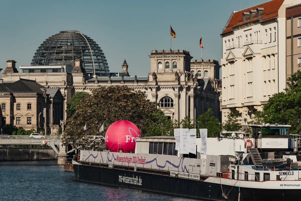 Die MS Wissenschaft im Wissenschaftsjahr 2024 liegt in Berlin-Mitte, im Hintergrund sieht man den Reichstag.