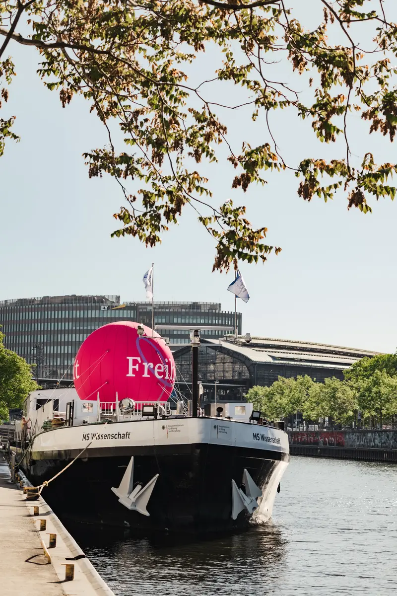 Außenansicht der MS Wissenschaft im Wissenschaftsjahr 2024 - Freiheit. Auf dem schwarz lackierten Schiff ist ein pinker Ballon zu sehen, auf dem "Freiheit" steht.