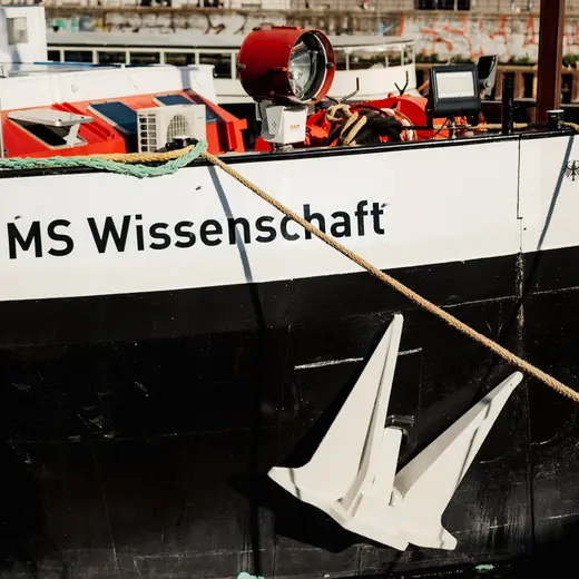 Nahaufnahme von einem angedockten Schiff. Ein großer Schriftzug "MS Wissenschaft" ist auf der Schiffseite lesbar.